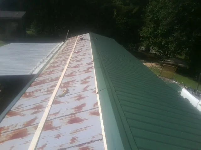 Old rusted panels beside newly installed green metal roofing — Wind Damage Roof Repair by Roofing Brothers in Perkinsville