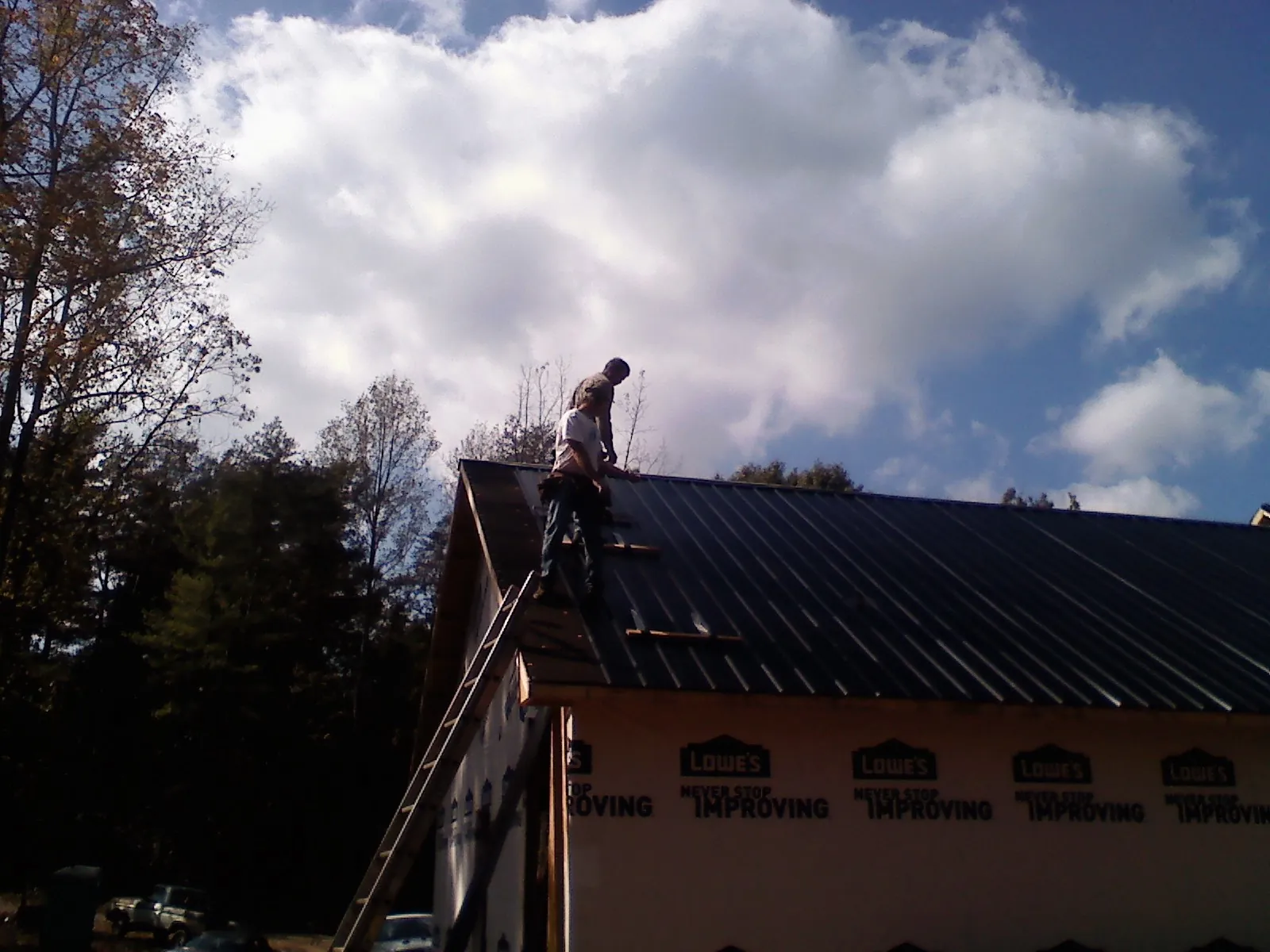 Roofer fastening dark metal panels high against a cloudy sky, from a Roof Inspection job in Perkinsville