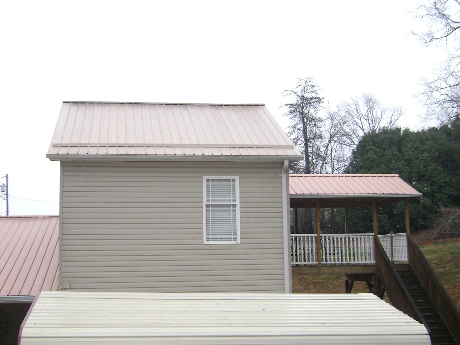 Tan metal roofs on a two story addition and attached porch, from a Roof Replacement job in Perkinsville